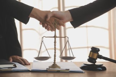Avukat, müvekkil ile evraklar, sözleşmeler, anlaşmalar, iş birliği anlaşmaları hakkında el sıkışıyor avukatın masasında bir kadın müvekkil ve masada bir çekiç.