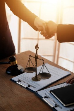 Avukat, müvekkil ile evraklar, sözleşmeler, anlaşmalar, iş birliği anlaşmaları hakkında el sıkışıyor avukatın masasında bir kadın müvekkil ve masada bir çekiç.