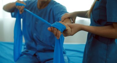 Hasta esnek bir egzersiz bandıyla esneme egzersizi yapıyor ve klinikte yardımcı olmak için fizyoterapist eli kullanıyor..