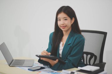 Güzel Asyalı iş kadını, ofise yerleştirilmiş evraklarla birlikte tablet ve dizüstü bilgisayar kullanıyor..