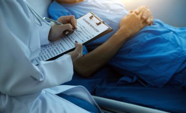 Doktor nabzını kontrol ederken hastanede yatan bir adam. Kadın doktor, erkek hastayı hastane odasında muayene ediyor..