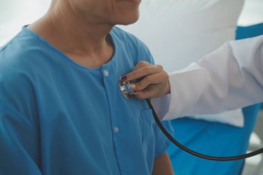 Doktor, hastane odasında muayene sırasında yaşlı adamın kalbini dinlemek için steteskop kullanıyor ve Coronavirus 'a karşı güvenlik önlemi olarak vizör takıyor. Enfeksiyonlar ve hastalıklar için tıbbi kontrol.