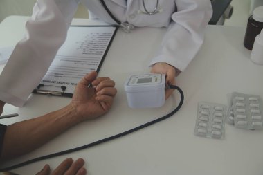 Steteskopla sfenometre kullanan bir doktor hastanede kan basıncını ölçüyor..