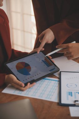 Group of confident business people point to graphs and charts to analyze market data, balance sheet, account, net profit to plan new sales strategies to increase production capacity.