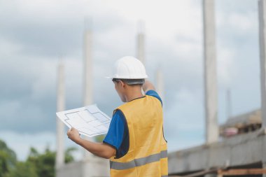 İnşaat alanındaki Mühendislik Danışmanlığı elinde planları tutuyor. İnşaat müfettişi. Yeni binanın inşaat sahası çizimi ve iş akışı