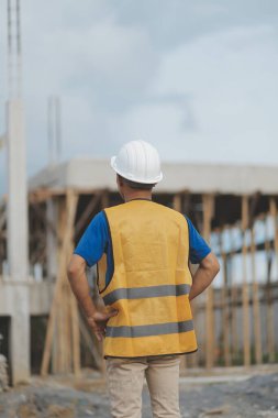 Asyalı mimar gökdelen arka planına sahip. Asyalı erkek mimar mühendis tasarımı. İnşaat alanında güvenli bir şekilde planlama yapıyor..