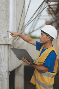 Genç yakışıklı Asyalı inşaat mühendisi elinde tabletle ileriye bakıyor ve düşünüyor, inşaat geçmişini planlıyor. Evrim inşa kavramı.