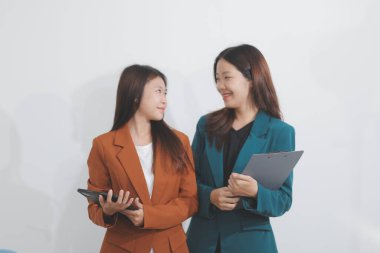 İki Kafkasyalı iş kadını, arka planda çeşitli görevlerde bulunan meslektaşlarıyla modern ofis ortamında bir tablet kullanarak birlikte çalışırlar..