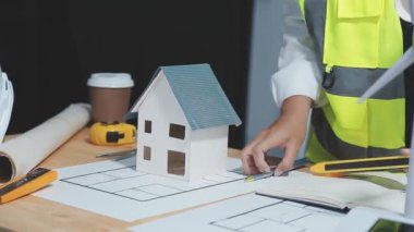 Ev inşaatında çalışan inşaat mühendisi, mimar konsepti, masanın üzerindeki plan, mimar veya mühendis ev modeliyle çalışıyor..