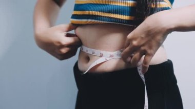 Karnında bantla belini ölçen bir kadın.