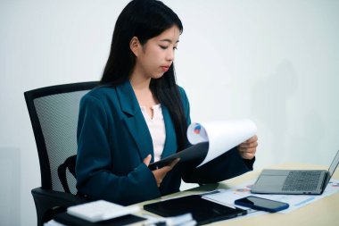 Asyalı iş kadını dizüstü bilgisayarla çalışıyor, pazarlama raporu ve hesap makinesi dokümanı masanın üzerinde, finansal raporları analiz etmek için online iş planına, e-ticarete yatırım yapıyor..