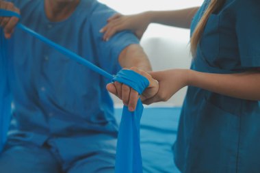 Hasta esnek bir egzersiz bandıyla esneme egzersizi yapıyor ve klinikte yardımcı olmak için fizyoterapist eli kullanıyor..
