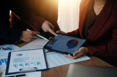 Group of confident business people point to graphs and charts to analyze market data, balance sheet, account, net profit to plan new sales strategies to increase production capacity.