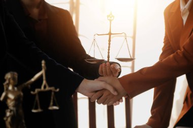 Avukat, müvekkil ile evraklar, sözleşmeler, anlaşmalar, iş birliği anlaşmaları hakkında el sıkışıyor avukatın masasında bir kadın müvekkil ve masada bir çekiç.