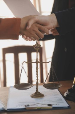Avukat, müvekkil ile evraklar, sözleşmeler, anlaşmalar, iş birliği anlaşmaları hakkında el sıkışıyor avukatın masasında bir kadın müvekkil ve masada bir çekiç.