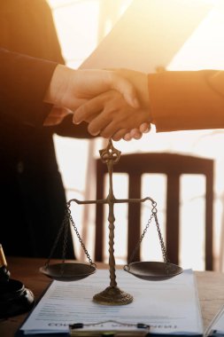 Avukat, müvekkil ile evraklar, sözleşmeler, anlaşmalar, iş birliği anlaşmaları hakkında el sıkışıyor avukatın masasında bir kadın müvekkil ve masada bir çekiç.