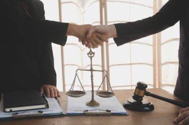 Avukat, müvekkil ile evraklar, sözleşmeler, anlaşmalar, iş birliği anlaşmaları hakkında el sıkışıyor avukatın masasında bir kadın müvekkil ve masada bir çekiç.