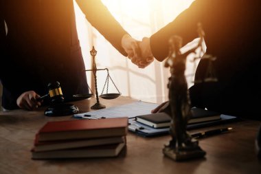 Avukat, müvekkil ile evraklar, sözleşmeler, anlaşmalar, iş birliği anlaşmaları hakkında el sıkışıyor avukatın masasında bir kadın müvekkil ve masada bir çekiç.