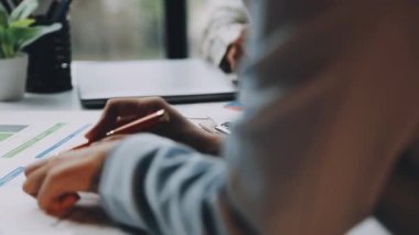 Bir grafiği hesaplamak ve tablodaki grafikleri analiz etmek için hesap makinesi kullanan bir iş adamı..