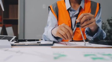 Dizüstü bilgisayarda çalışan ve ofisteki planlara çizim yapan mühendis.