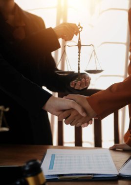 Avukat, müvekkil ile evraklar, sözleşmeler, anlaşmalar, iş birliği anlaşmaları hakkında el sıkışıyor avukatın masasında bir kadın müvekkil ve masada bir çekiç.