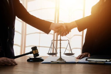 Avukat, müvekkil ile evraklar, sözleşmeler, anlaşmalar, iş birliği anlaşmaları hakkında el sıkışıyor avukatın masasında bir kadın müvekkil ve masada bir çekiç.