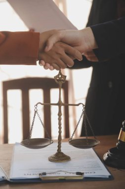 Avukat, müvekkil ile evraklar, sözleşmeler, anlaşmalar, iş birliği anlaşmaları hakkında el sıkışıyor avukatın masasında bir kadın müvekkil ve masada bir çekiç.
