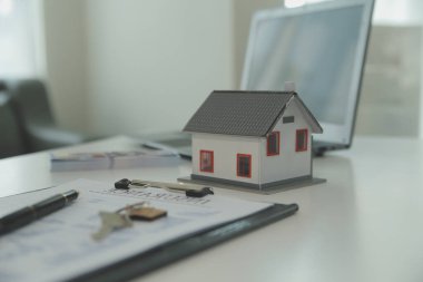 Emlakçı emlakçı ev modelini işaret eden bir kalem kullanıyor ve iş sözleşmesini, kirayı, satın almayı, ipoteği, krediyi veya ev sigortasını açıklıyor