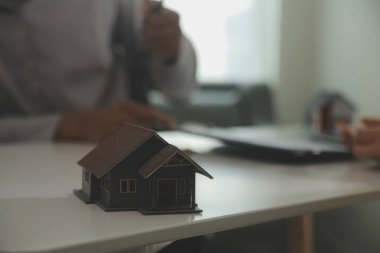 Emlakçı emlakçı ev modelini işaret eden bir kalem kullanıyor ve iş sözleşmesini, kirayı, satın almayı, ipoteği, krediyi veya ev sigortasını açıklıyor