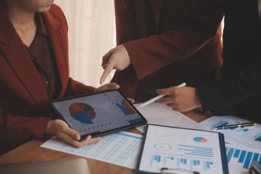 Group of confident business people point to graphs and charts to analyze market data, balance sheet, account, net profit to plan new sales strategies to increase production capacity.