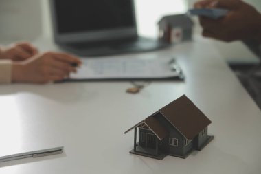 Emlakçı emlakçı ev modelini işaret eden bir kalem kullanıyor ve iş sözleşmesini, kirayı, satın almayı, ipoteği, krediyi veya ev sigortasını açıklıyor