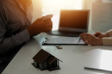 Emlakçı emlakçı ev modelini işaret eden bir kalem kullanıyor ve iş sözleşmesini, kirayı, satın almayı, ipoteği, krediyi veya ev sigortasını açıklıyor