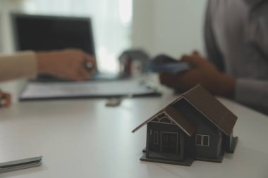 Emlakçı emlakçı ev modelini işaret eden bir kalem kullanıyor ve iş sözleşmesini, kirayı, satın almayı, ipoteği, krediyi veya ev sigortasını açıklıyor