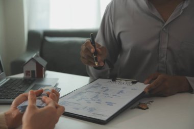 Emlakçı emlakçı ev modelini işaret eden bir kalem kullanıyor ve iş sözleşmesini, kirayı, satın almayı, ipoteği, krediyi veya ev sigortasını açıklıyor
