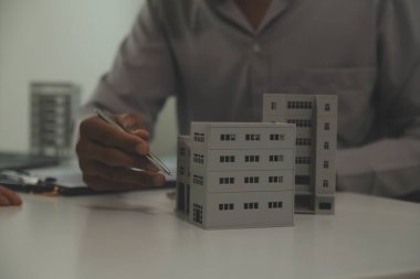 Emlakçı emlakçı ev modelini işaret eden bir kalem kullanıyor ve iş sözleşmesini, kirayı, satın almayı, ipoteği, krediyi veya ev sigortasını açıklıyor