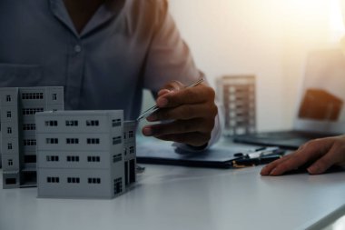 Emlakçı emlakçı ev modelini işaret eden bir kalem kullanıyor ve iş sözleşmesini, kirayı, satın almayı, ipoteği, krediyi veya ev sigortasını açıklıyor