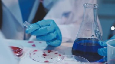 Mavi eldivenli ve koruyucu eldivenli bir bilim adamının elinde bir şişe sıvı tutarken...