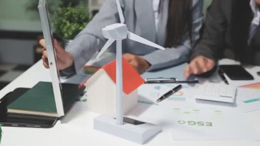 İş adamı enerji modelini tutuyor ve ofis masasında güneş enerjisi sistemli akıllı tablet kullanıyor.