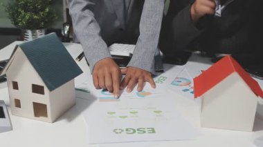 Emlakçı müşterilere ev modelini, emlakçıyı, sigortayı ve yatırım konseptini gösteriyor.