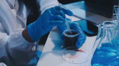 Mavi üniformalı bilim adamı elinde test tüpü ve kimyasal çözelti tutuyor.