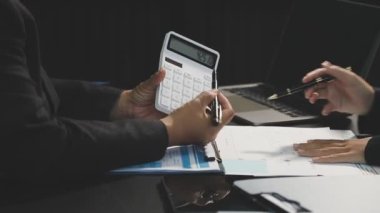 İş adamı, masadaki mali raporu analiz etmek için hesap makinesi kullanıyor..