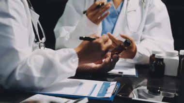 Beyaz önlüklü ve siyah ceketli bir doktor arka planda elleri olan bir kalem tutuyor.