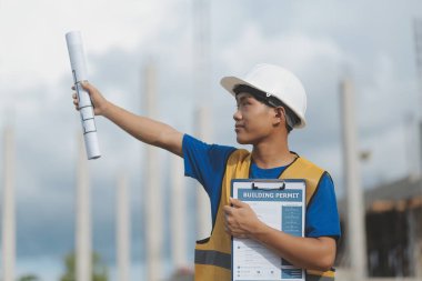 İnşaat alanındaki miğferli ve planlı mühendis elinde