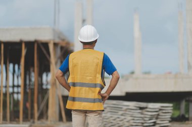 Asyalı mimar gökdelen arka planına sahip. Asyalı erkek mimar mühendis tasarımı. İnşaat alanında güvenli bir şekilde planlama yapıyor..