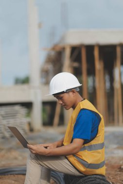 Asyalı mimar gökdelen arka planına sahip. Asyalı erkek mimar mühendis tasarımı. İnşaat alanında güvenli bir şekilde planlama yapıyor..