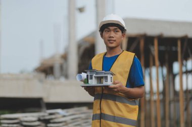 Genç yakışıklı Asyalı inşaat mühendisi elinde tabletle ileriye bakıyor ve düşünüyor, inşaat geçmişini planlıyor. Evrim inşa kavramı.