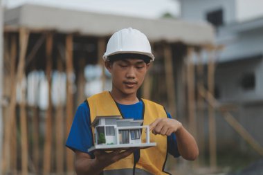 Genç yakışıklı Asyalı inşaat mühendisi elinde tabletle ileriye bakıyor ve düşünüyor, inşaat geçmişini planlıyor. Evrim inşa kavramı.