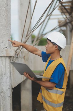 Genç yakışıklı Asyalı inşaat mühendisi elinde tabletle ileriye bakıyor ve düşünüyor, inşaat geçmişini planlıyor. Evrim inşa kavramı.
