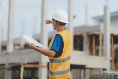 İnşaat alanındaki Mühendislik Danışmanlığı elinde planları tutuyor. İnşaat müfettişi. Yeni binanın inşaat sahası çizimi ve iş akışı