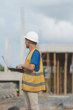 Dizüstü bilgisayarı tutan işçi ya da mühendis ve deponun içindeki konteynırları kontrol ediyor